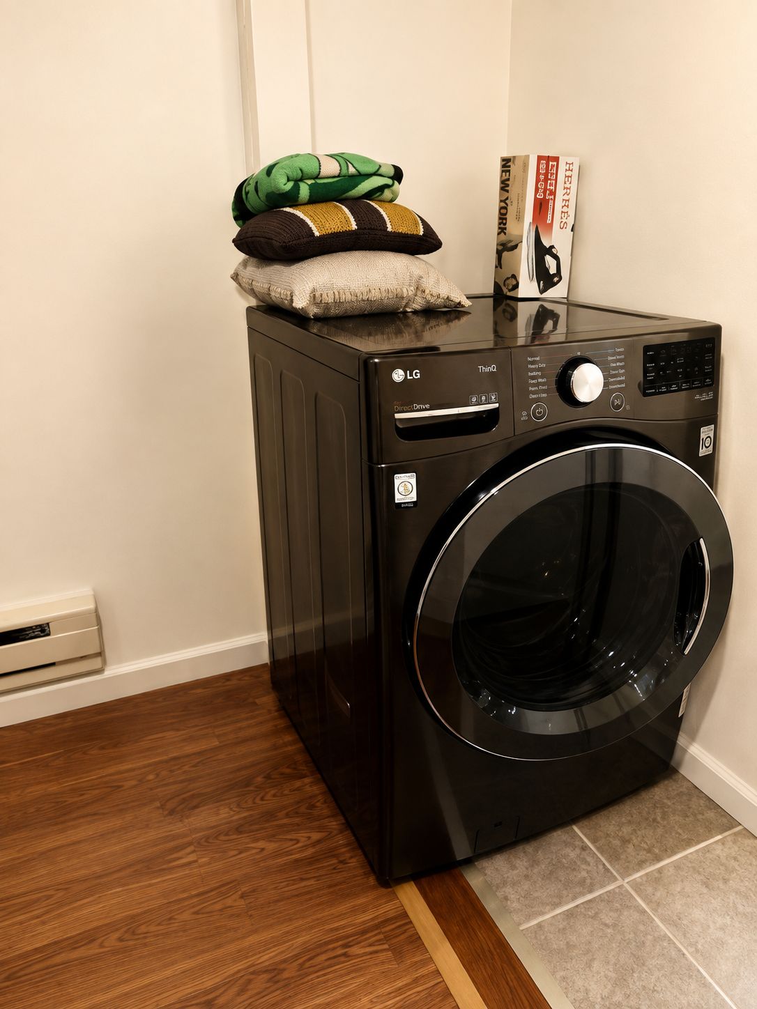 A black LG Direct Drive washing machine with a control panel, a pillow, and a magazine on top.
