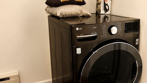 A black LG Direct Drive washing machine with a control panel, a pillow, and a magazine on top.