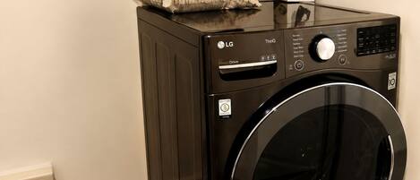 A black LG Direct Drive washing machine with a control panel, a pillow, and a magazine on top.