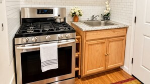 A compact kitchen with a stainless steel stove, wooden cabinets, a white tiled backsplash, and a wooden floor.