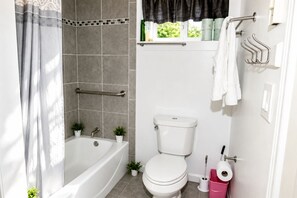 Et badeværelse med badekar, toilet og et vindue med gardiner.
