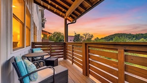 Eine Holzterrasse mit Gartenmöbeln, Blick auf die Landschaft und einem Sonnenuntergang.