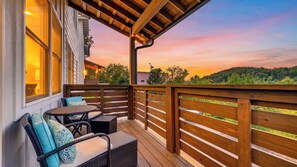 Una terraza de madera con mobiliario exterior, vistas del paisaje y un atardecer.
