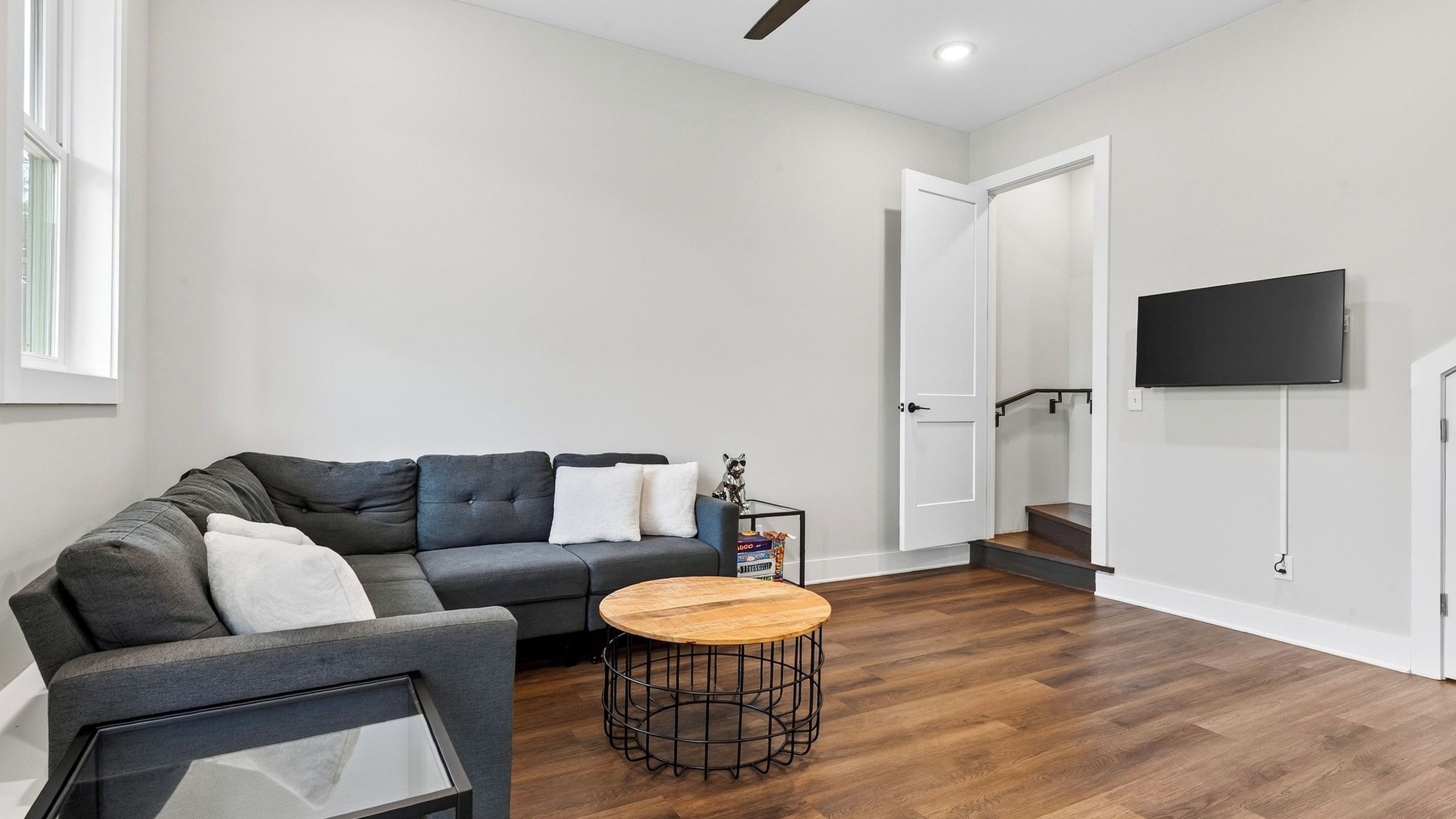 A modern living room with a grey sofa, a small round coffee table, and a flat-screen TV mounted on the wall.
