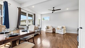 Amplia sala de estar con una mesa de comedor de madera dispuesta para dos personas, un sofá, dos sillones y un ventilador de techo.
