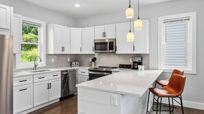 A modern kitchen with white cabinetry, stainless steel appliances, and a central island with bar stools. - Tranquil River Home by Avantstay Blue Ridge Views + Balcony + Two Living Rooms Mins to Downtown (Asheville)