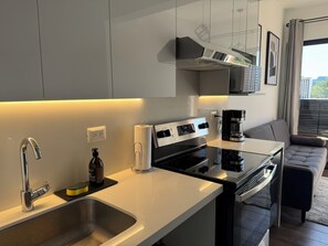 A modern kitchen with a stainless steel sink, a black stove, and a coffee maker. - Luxury One-Bedroom, City Views, Pool & A/C (Ciudad de Guatemala)
