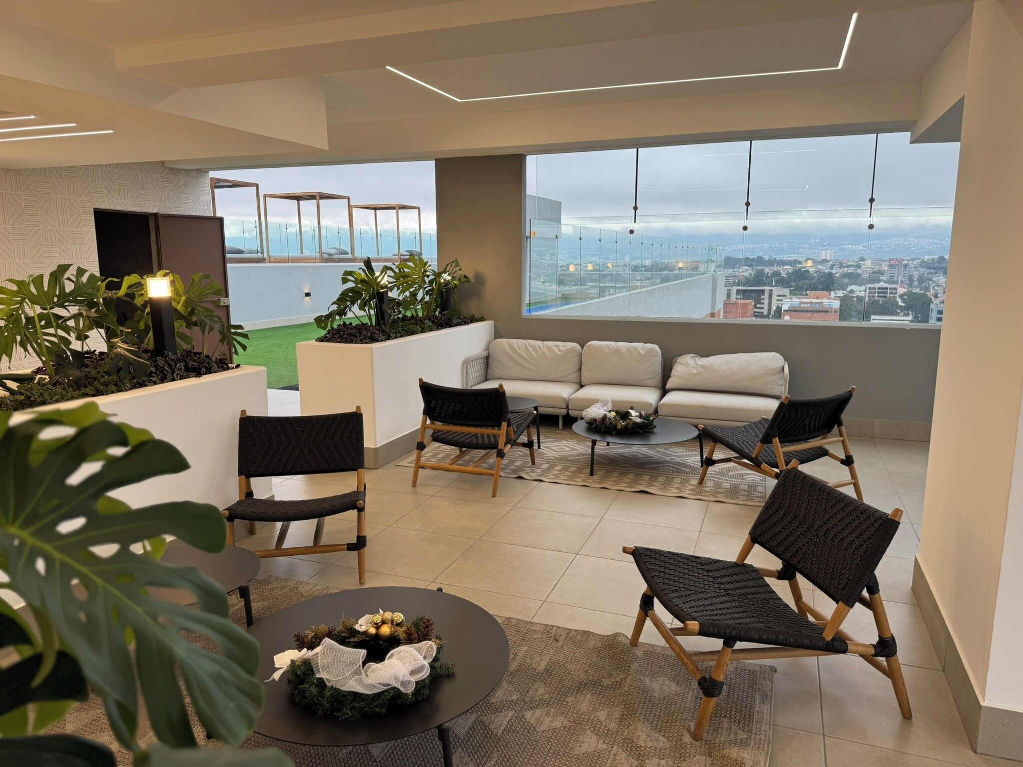 Ein stilvoller Lounge-Bereich mit einer Couch, Sesseln und einem kleinen Tisch, mit Blick auf die Stadt durch große Fenster.