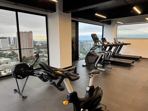 A gym with cardio equipment, large windows, and a city view. - Luxury One-Bedroom, City Views, Pool & A/C (Ciudad de Guatemala)