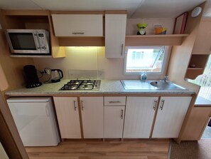 A compact kitchen with a microwave, stove, sink, and a window providing natural light.