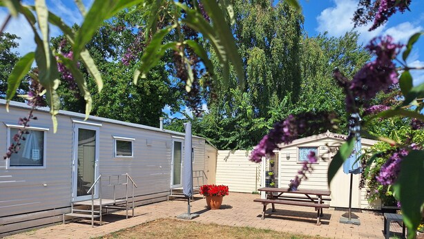 Een stacaravan met een terras, een kleine tuin en een picknicktafel.