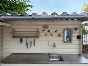 Eine Küche mit einem Edelstahl-Spülbecken, einem Holzregal und einem Fenster mit Spiegel.