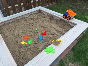 Ein Sandkasten mit verschiedenen Spielsachen und einem Spielzeug-Muldenkipper.