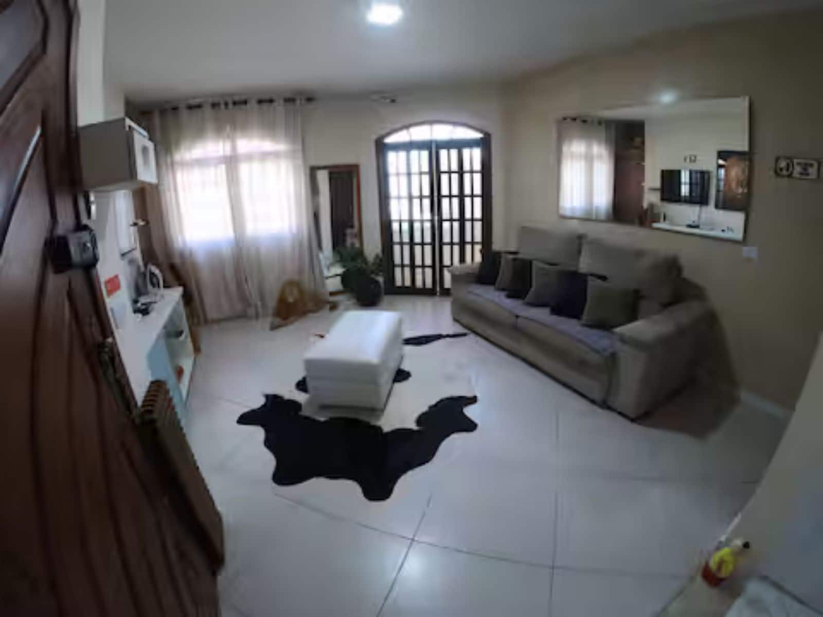 Una sala de estar con un sofá, un reposapiés y un ventanal con cortinas.