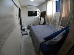 Quarto com cama, mesa de cabeceira, espelho e janela.