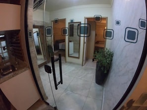 Un baño con puerta de cristal, lavamanos, espejo y una planta en maceta.