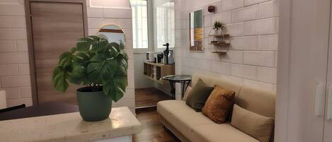 A living room with a sofa, a coffee table, a potted plant, and a kitchen area with a microwave and toaster.