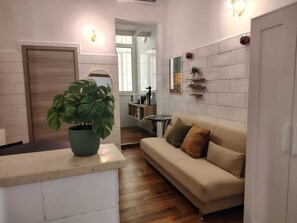 Una sala de estar con sofá, una mesa de centro, una planta en maceta y una zona de cocina con microondas y tostadora.