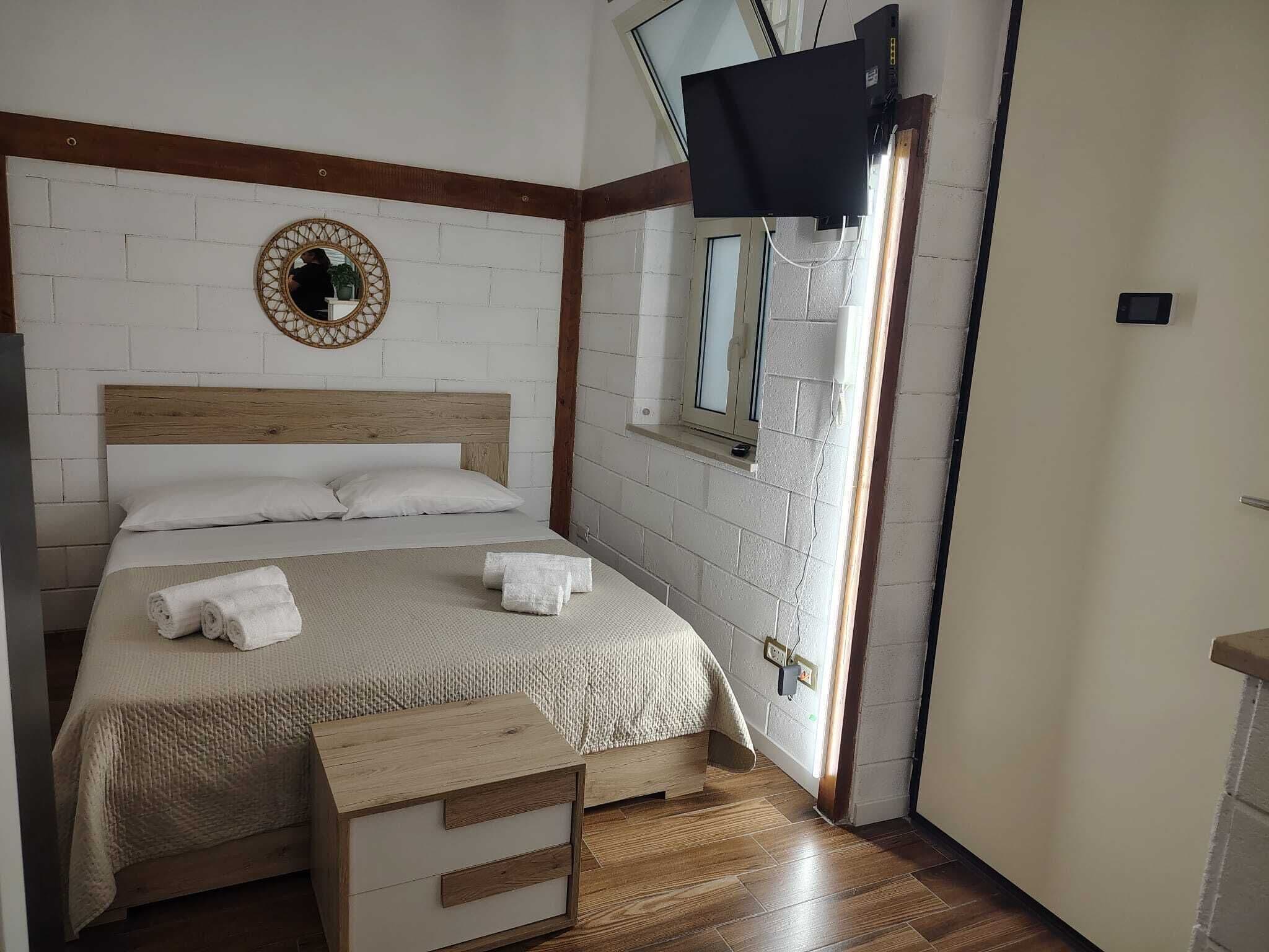 A bedroom with a bed, a TV mounted on the wall, a window, and a wooden headboard.