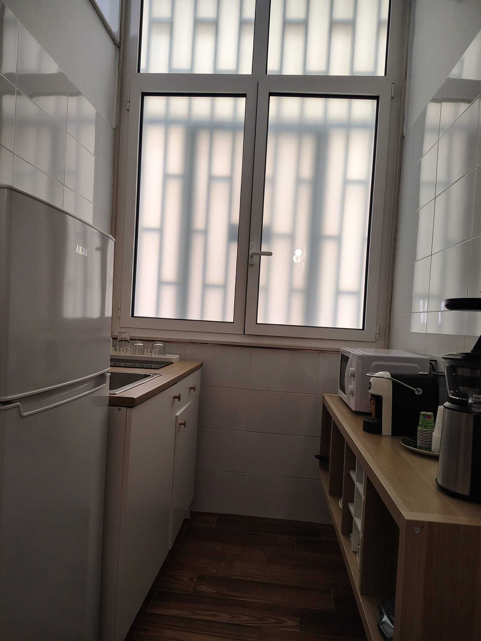Una cucina compatta con finestra, lavandino, pensili e un piano di lavoro con elettrodomestici.
