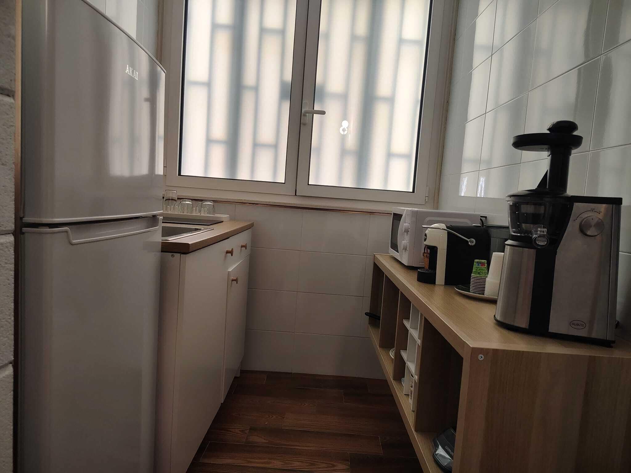 Een functionele keuken met een koelkast, een spoelbak, een magnetron en een koffiezetapparaat.