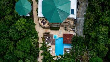 An aerial view of a property with multiple swimming pools, a large central building with a green roof, and surrounding lush greenery.