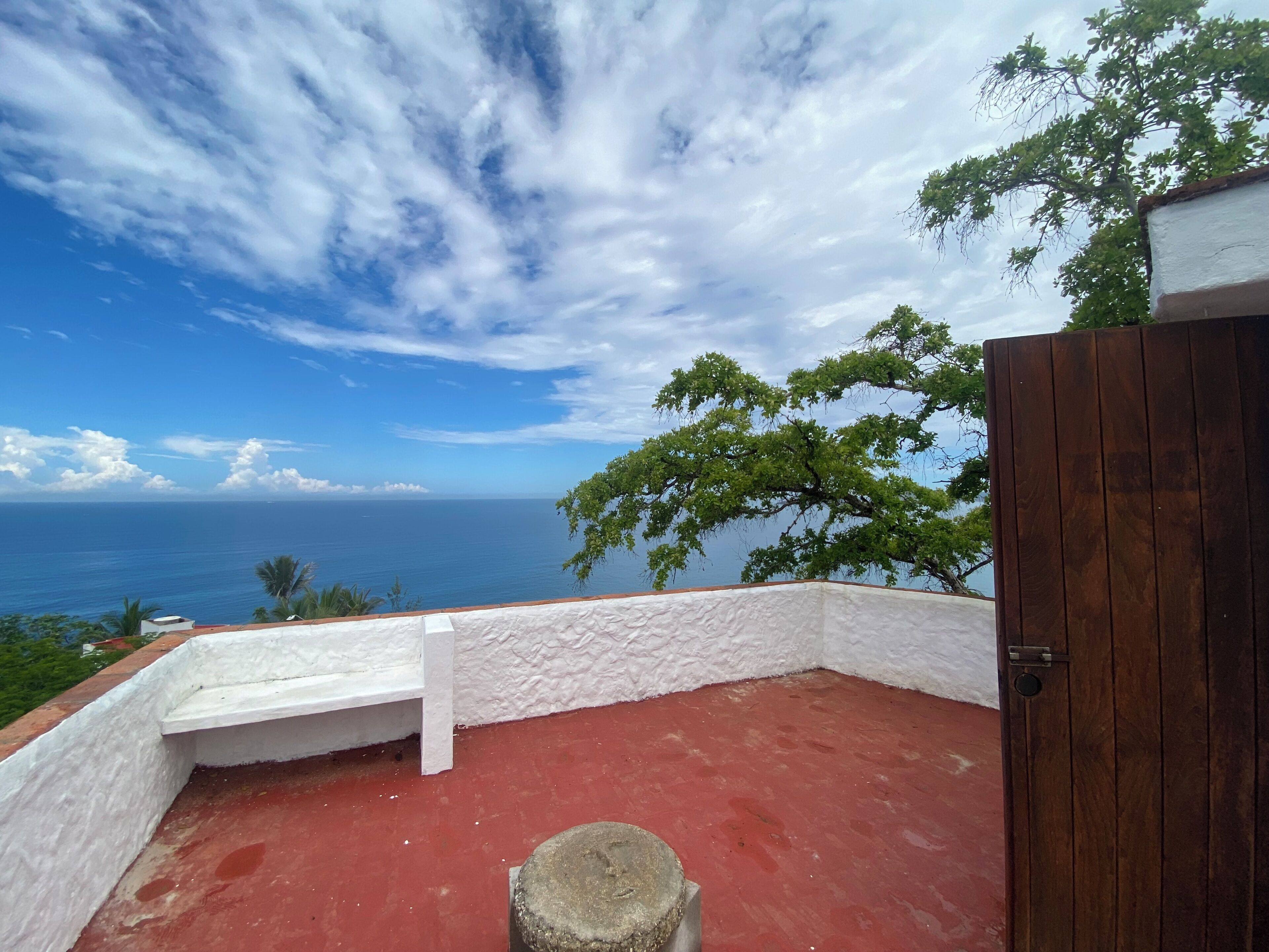 A balcony with a red floor, white walls, and a view of the ocean.