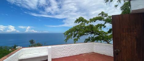 A balcony with a red floor, white walls, and a view of the ocean.