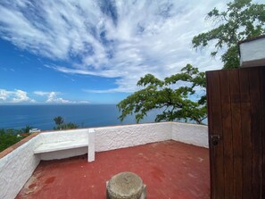 Un balcón con piso rojo, paredes blancas y vista al océano.