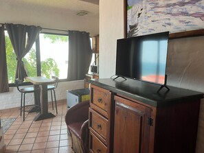 A room with a television on a wooden cabinet, a small table, a chair, and a window with curtains. - Montebello, apartments with spectacular ocean views. (Mazatlán)