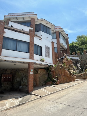 A multi-story building with a white facade and red brick accents, featuring large windows and a stone foundation. - Montebello, apartments with spectacular ocean views. (Mazatlán)