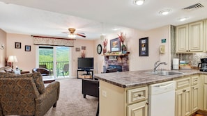 A spacious living room with a large sofa, a dining area with a table, and a kitchen with a built-in dishwasher. - Lazy Bear by Avantstay Mountain-view Condo Shared Pool + Hot Tub + Sauna Near Gatlinburg (Gatlinburg)