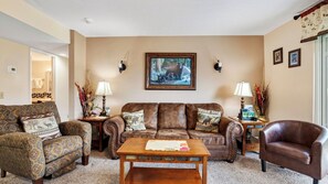 A living room with a brown leather sofa, patterned armchairs, a wooden coffee table, and a painting of a bear on the wall. - Lazy Bear by Avantstay Mountain-view Condo Shared Pool + Hot Tub + Sauna Near Gatlinburg (Gatlinburg)