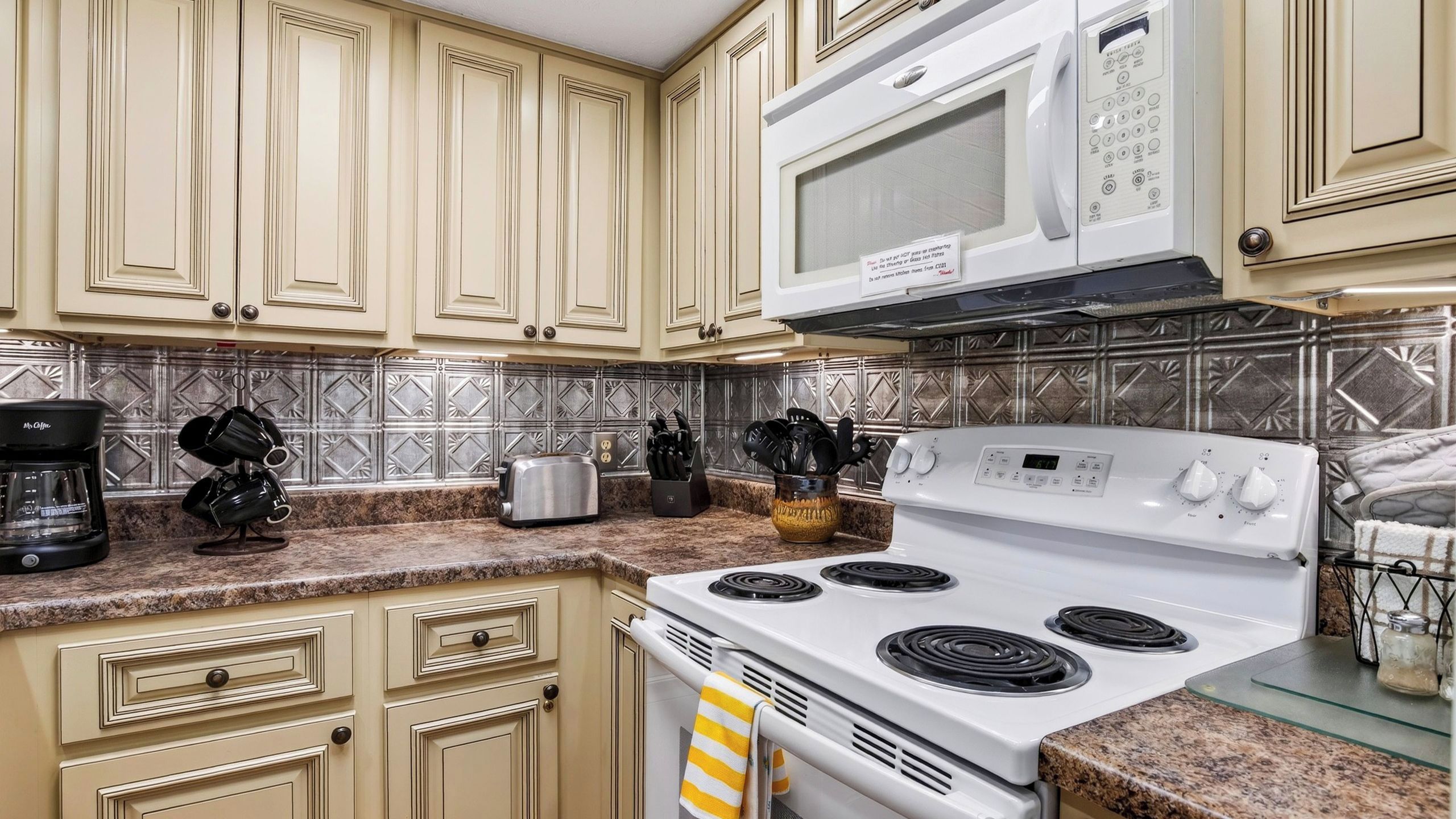 Una cocina con armarios color beige, estufa blanca, microondas y cafetera.