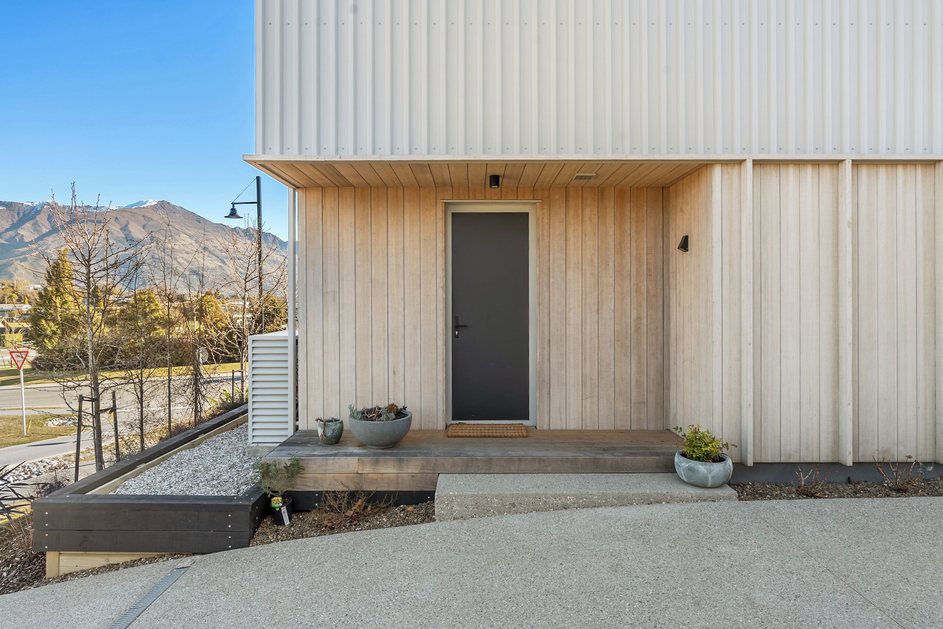 A modern building with a wooden facade, a dark door, and a small porch with potted plants.