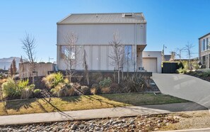 A modern building with a flat roof, a large window, and a paved driveway. - Architecturally Designed - Wanaka Holiday Home (Wanaka)