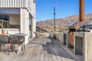 A wooden deck with outdoor furniture, a barbecue grill, and a view of mountains in the background. - Architecturally Designed - Wanaka Holiday Home (Wanaka)