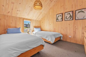 A wooden-paneled bedroom with two beds, a hanging light fixture, and three framed pictures on the wall. - Architecturally Designed - Wanaka Holiday Home (Wanaka)