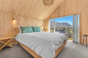 A bedroom with a large bed, wooden walls, a view of mountains, and a sliding glass door. - Architecturally Designed - Wanaka Holiday Home (Wanaka)