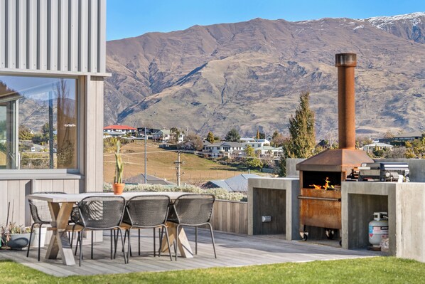 An outdoor patio with a table and chairs, a chimney, and a view of a mountain range. - Architecturally Designed - Wanaka Holiday Home (Wanaka)