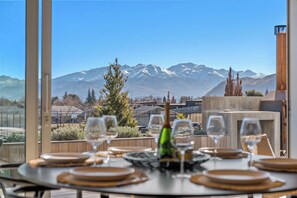 A dining table with wine glasses and a bottle, set against a backdrop of snow-capped mountains. - Architecturally Designed - Wanaka Holiday Home (Wanaka)