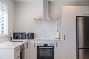 A modern kitchen with a Bosch oven, a microwave, a coffee maker, and a refrigerator. - The Cozy Koha - Taupo Holiday Home (Taupo)
