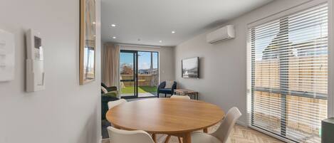 A modern dining area with a round table, chairs, and a view of a backyard through a sliding glass door.