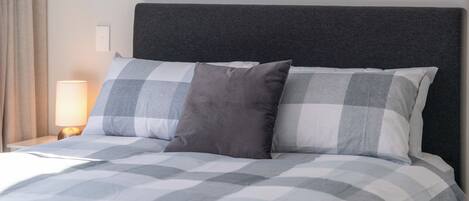 A bed with a checkered bedspread, two pillows, a bedside lamp, and a dark headboard.