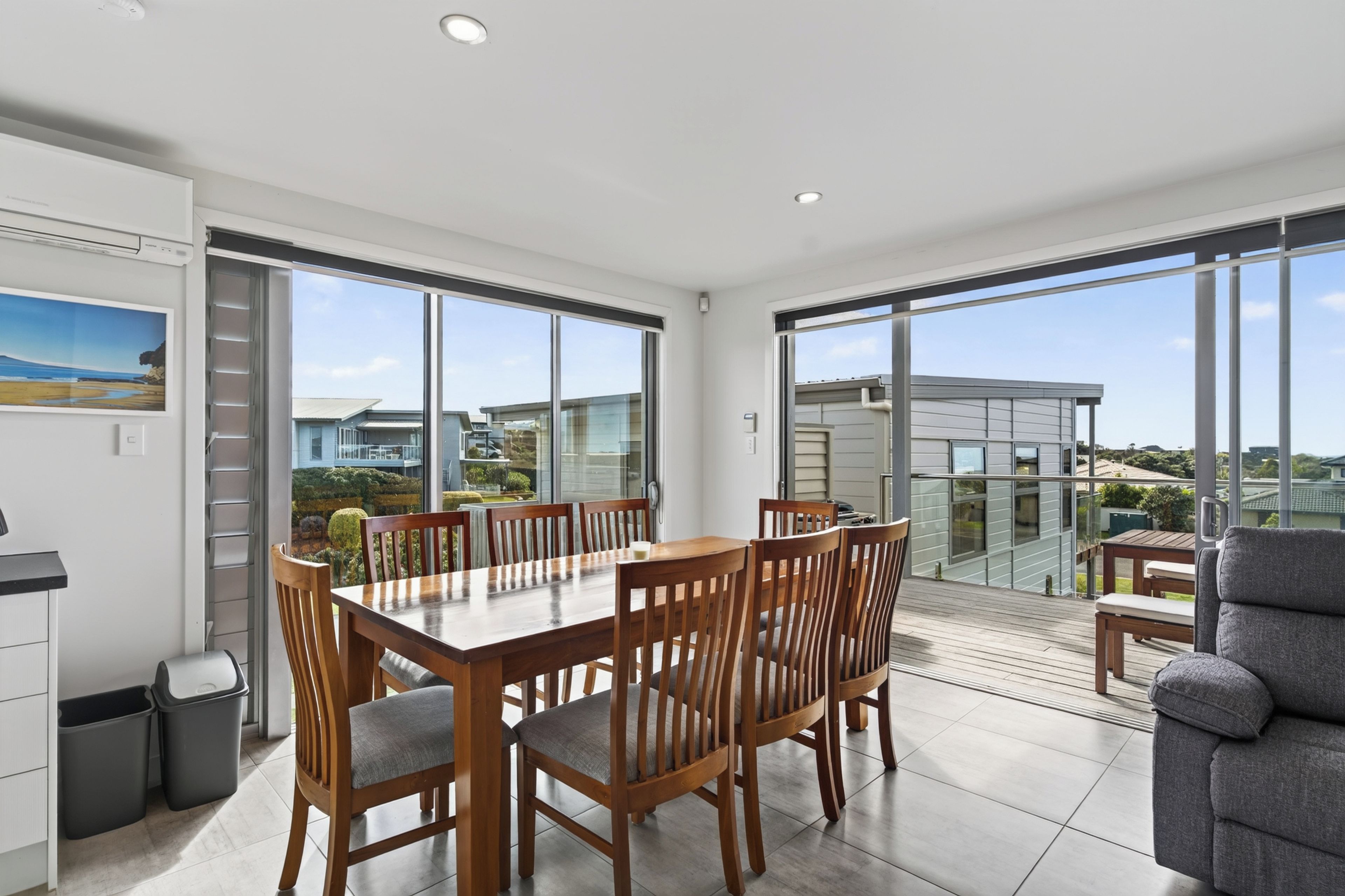 A spacious dining area with a large table and chairs, large windows offering a view of the surrounding area, and a balcony with a view of the neighborhood.