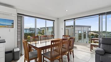 A spacious dining area with a large table and chairs, large windows offering a view of the surrounding area, and a balcony with a view of the neighborhood.