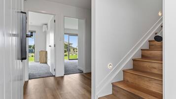 A modern interior with a wooden staircase, a hallway leading to a door, and a view of the outdoors.