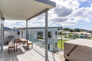 A modern outdoor deck with a table and chairs, glass railings, and a view of the neighborhood. - Starling - Mangawhai Heads Holiday Home (Mangawhai)