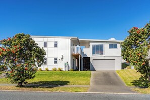 A modern two-story residential building with a garage, a covered porch, and a well-maintained lawn. - Starling - Mangawhai Heads Holiday Home (Mangawhai)