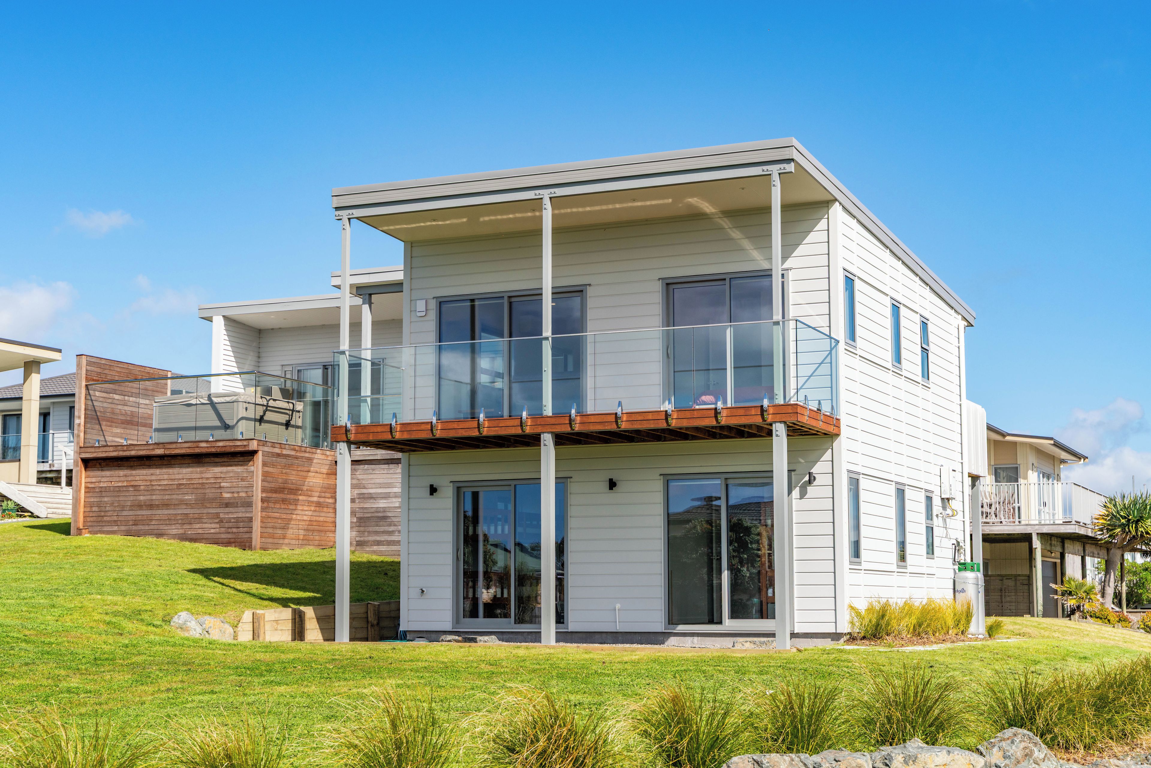 A modern two-story house with a balcony, large windows, and a well-maintained lawn.